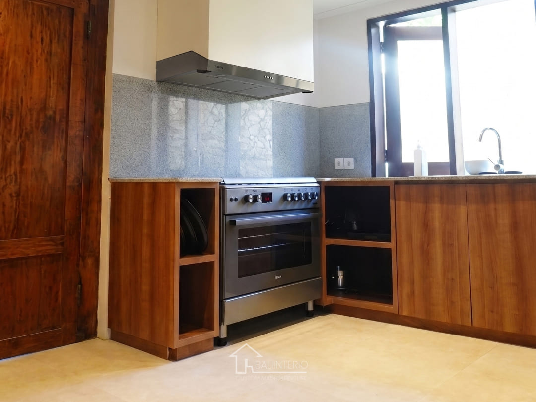 Custom kitchen set in Villa Ambar Ungasan featuring warm wood HPL cabinets, stainless range hood, and granite backsplash by Bali Interio
